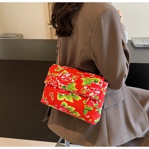 Detail of red floral canvas crossbody bag with metal chain strap on minimalist blazer