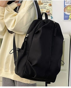 Detail view of the black nylon backpack side pocket with drawstring and woven zipper pull