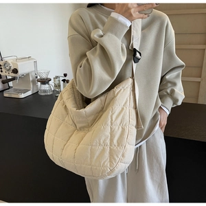 Detail of a beige quilted moon-shaped puffer bag shown in a cozy coffee shop setting