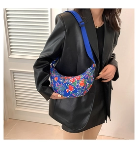Blue crescent shoulder bag with red floral print shown on model with adjustable strap