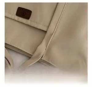Detail view of stitched brown leather logo tag on beige canvas tote bag material