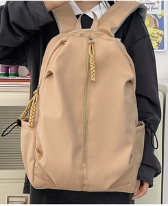 Close-up of khaki nylon backpack featuring woven zipper pulls and side drawstring pockets