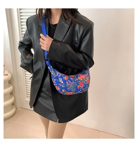 Blue crescent nylon crossbody bag with red floral print shown on model in modern room