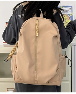 Detail of minimalist beige nylon backpack featuring woven rope zipper and side drawstring pockets