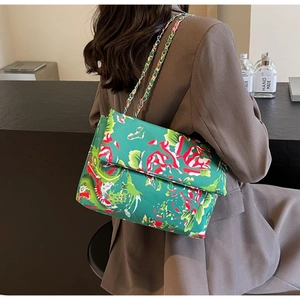 Detail of green dragon floral print satchel with gold chain strap on shoulder