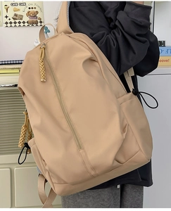 Detail view of stylish beige nylon backpack with vertical zipper and woven puller detail