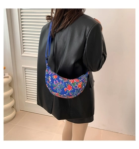 Blue half-moon crossbody bag with traditional floral pattern and wide nylon shoulder strap