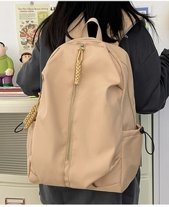 Detail view of beige nylon backpack featuring a sleek vertical zipper and woven puller