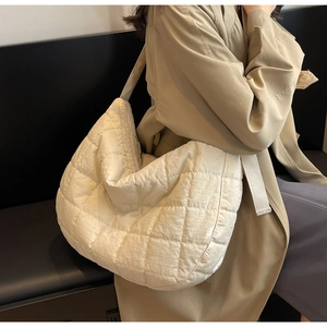 Close-up of beige quilted crossbody bag with puffer texture on a beige coat model