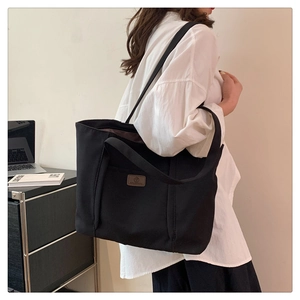 Detailed side view of a minimalist black canvas tote bag being worn by a fashion model