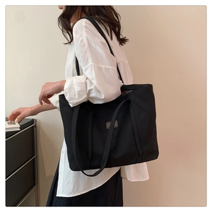 Detail of a black canvas tote bag showing thick shoulder straps and a grey leather logo