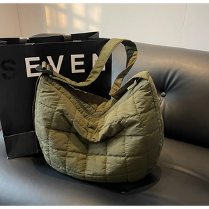 Olive green quilted nylon crescent crossbody bag with large capacity on a black leather sofa