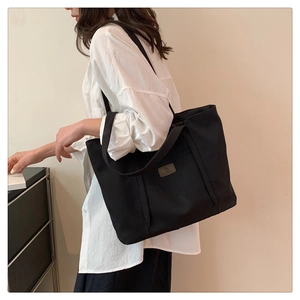 Close-up of a large black canvas tote bag worn by a model in a minimalist setting