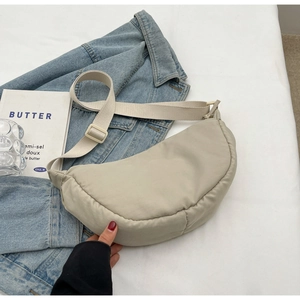 Fashionable quilted crescent crossbody bag made of beige nylon fabric on denim background