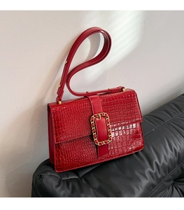 Macro shot of red crossbody bag with crocodile pattern and golden metal chain buckle