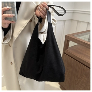 Detail of a black suede tote bag with leather handles shown in a minimalist setting