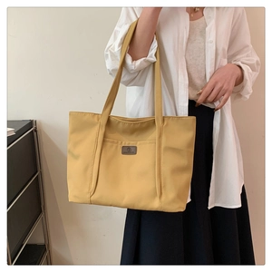Detail of mustard yellow canvas tote bag featuring front pocket and logo patch