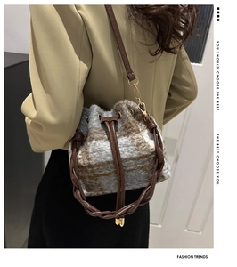 Detail of grey plaid textured bucket bag with brown faux leather drawstring and strap