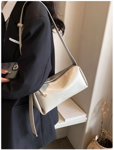 Close-up of stylish off-white cylindrical shoulder bag on a black blazer