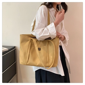 Detail of a yellow canvas tote bag featuring a small front pocket and dark leather logo label