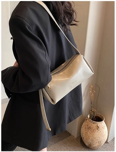 Close-up of minimalist cream cylindrical PU leather crossbody bag worn on shoulder