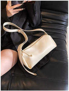 Detail showing the embossed logo and smooth leather texture of a cream crossbody bag