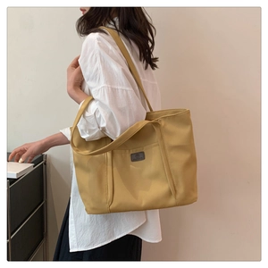 Detail of a ginger yellow canvas tote bag with leather logo tag and dual handles