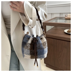 Detail of plaid faux fur bucket bag with drawstring closure and woven brown handle