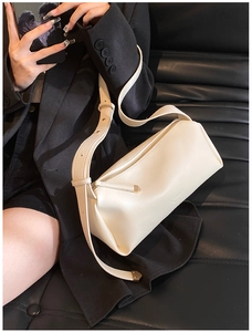 Close-up of cream cylinder crossbody bag with golden hardware and brand logo