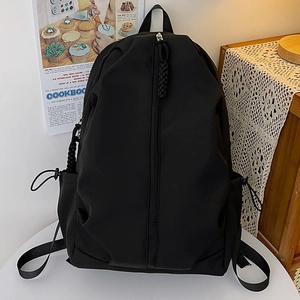 Minimalist black nylon fashion backpack with vertical zipper and woven puller on a desk