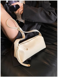Detail view of cream white PU leather crossbody bag with adjustable strap on a black background