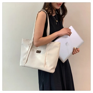 Detail of white nylon tote bag with leather logo tag holding a laptop for office use