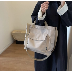 Close-up of beige canvas tote bag with large front flap pocket and woven FASHION label