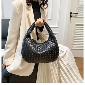 Close-up of a black woven leather Hobo handbag held by a model in a beige suit