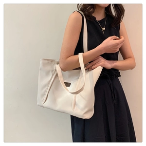White canvas tote bag featuring brown leather logo patch on shoulder for daily commute