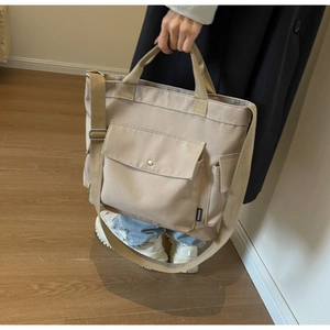 Detail view of stylish canvas tote bag showing front pocket with metal buckle and shoulder strap