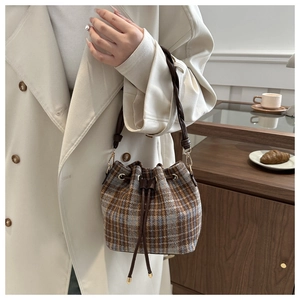 Close-up of a vintage plaid drawstring bucket bag with a woven leather handle and gold hardware