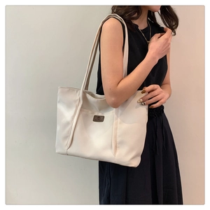 Close-up of minimalist cream canvas tote bag with contrast leather logo patch detail