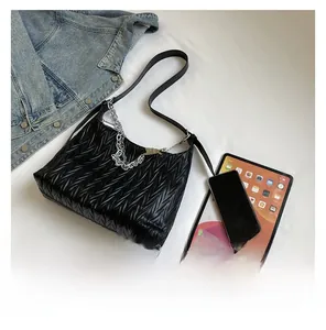 Detail of pleated PU leather bag with silver chain and rabbit charm next to an iPad