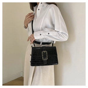Detail shot of black crocodile pattern faux leather handbag with elegant gold chain buckle