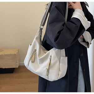 Detail of canvas shoulder bag showing front zipper pockets and woven texture