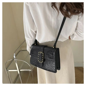 Detail shot of a black faux crocodile crossbody bag with golden chain buckle on a model