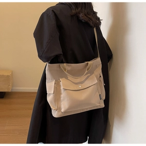 Detail view of a beige canvas tote bag showing side pockets and fashion tag