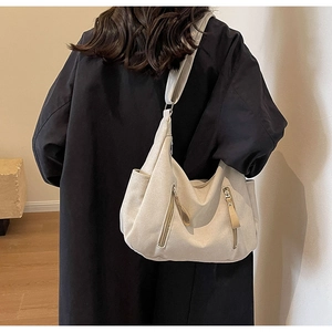 Minimalist cream canvas crossbody bag detail showing dual zippers on a model wearing black coat