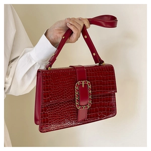 Detail of red-brown croc-embossed handbag with gold buckle and smooth chain accent