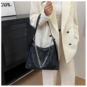Detailed view of black pleated PU shoulder bag with decorative silver chains on model