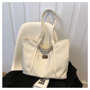 Minimalist off-white canvas tote bag with front pocket and brown leather logo patch