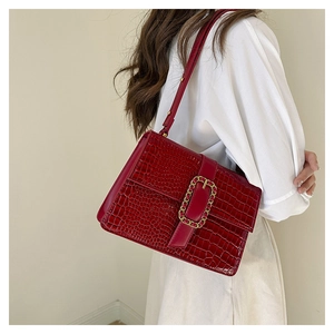Detail of burgundy crocodile-embossed leather bag with gold buckle on shoulder