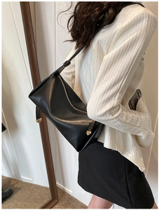Detail view of black geometric PU leather shoulder bag with gold hardware on a model