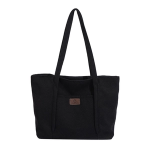 Minimalist black canvas tote bag with brown leather logo tag and dual shoulder straps